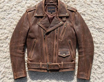 Könnte beinhalten: Eine braune Motorradjacke aus Distressed-Leder mit breitem Reverskragen, asymmetrischem Frontreißverschluss, mehreren Reißverschlusstaschen, einer kleinen Klappentasche mit Druckknopf, Schulterklappen und einem Gürtel mit Schnalle. Das Innenetikett zeigt Sk. Leather.