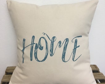 May include: A cream-colored throw pillow with the word "home" printed in a blue, brushstroke font.