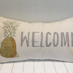 May include: A white pillow with a gray "WELCOME" message and a yellow pineapple illustration.