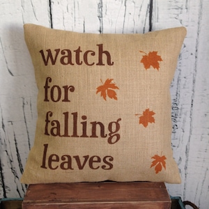 May include: A burlap pillow with the text "watch for falling leaves" and orange leaf designs.