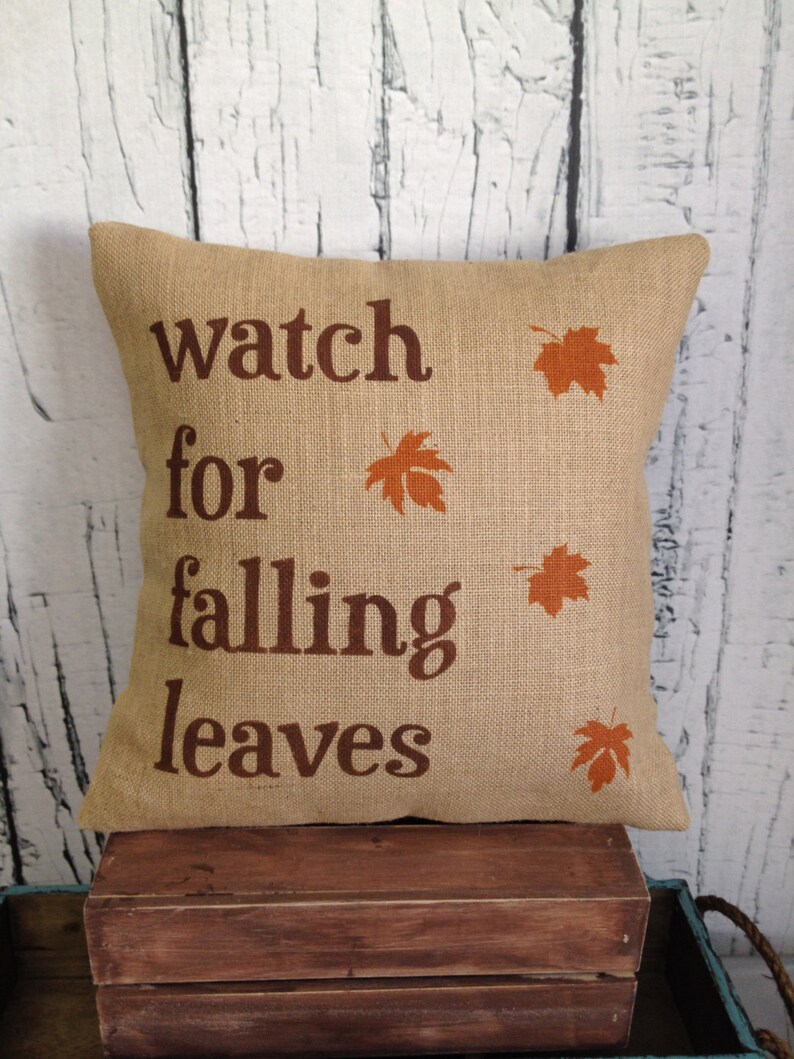 May include: A burlap pillow with the text "watch for falling leaves" and orange leaf designs.