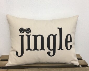 May include: A beige throw pillow with black text that reads "jingle" and two black bells on the left side.