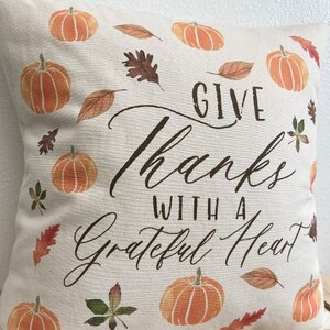 May include: A white throw pillow with a fall theme. It features a brown and orange pumpkin design, brown leaves, and the text "Give Thanks With A Grateful Heart".
