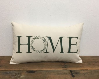 May include: A white pillow with the word "HOME" in black lettering. The "O" in home is a green wreath with leaves.