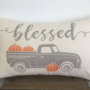 May include: A white pillow with the word "blessed" in gray script and a gray pickup truck carrying pumpkins. The truck is on a white background.