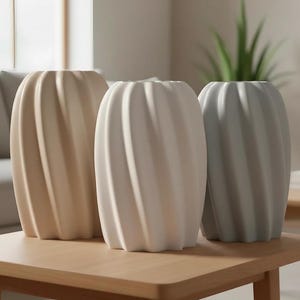 Può includere: Tre vasi in ceramica dai toni neutri sono su un tavolo di legno. I vasi hanno un design a coste a spirale e sono nelle tonalità del beige, bianco e grigio. Lo sfondo comprende una finestra, un divano e una pianta.
