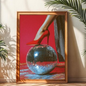 Può includere: Opera d'arte incorniciata con una scarpa con tacco rosso su una palla da discoteca. L'opera d'arte è ambientata su uno sfondo rosso. L'immagine è in una cornice di legno ed è esposta in una stanza con piante.
