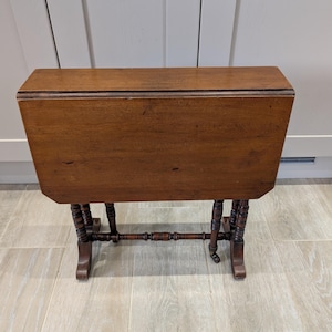 May include: A dark brown, vintage drop-leaf table. The rectangular table has rounded corners and decorative, turned legs. The table is approximately 76 cm long when open and 46 cm wide.