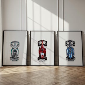 Puede incluir: Tres impresiones enmarcadas de coches de carreras de Fórmula 1. Los coches se representan desde arriba, mostrando sus diseños aerodinámicos. Los esquemas de color incluyen turquesa, rojo y azul, cada uno sobre un fondo blanco.
