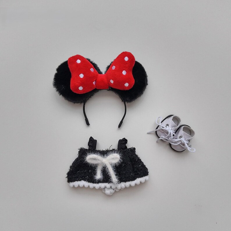 May include: A set of doll accessories, including a black headband with fuzzy ears and a red bow with white polka dots, a black skirt with a white bow, and a pair of white doll shoes.