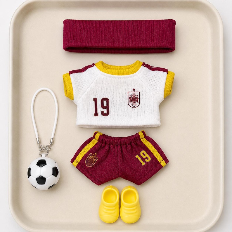 May include: A miniature sports kit comprising a white short-sleeved jersey with yellow trim and the number 19, maroon shorts with yellow stripes and the number 19, a maroon headband, yellow shoes, and a football keyring with a white loop.