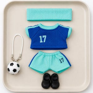 May include: A doll-sized sports outfit featuring a blue t-shirt with the number 17 in light blue, light blue mesh shorts with the number 17 in dark blue, a matching light blue mesh headband, a pair of black shoes, and a football key ring.