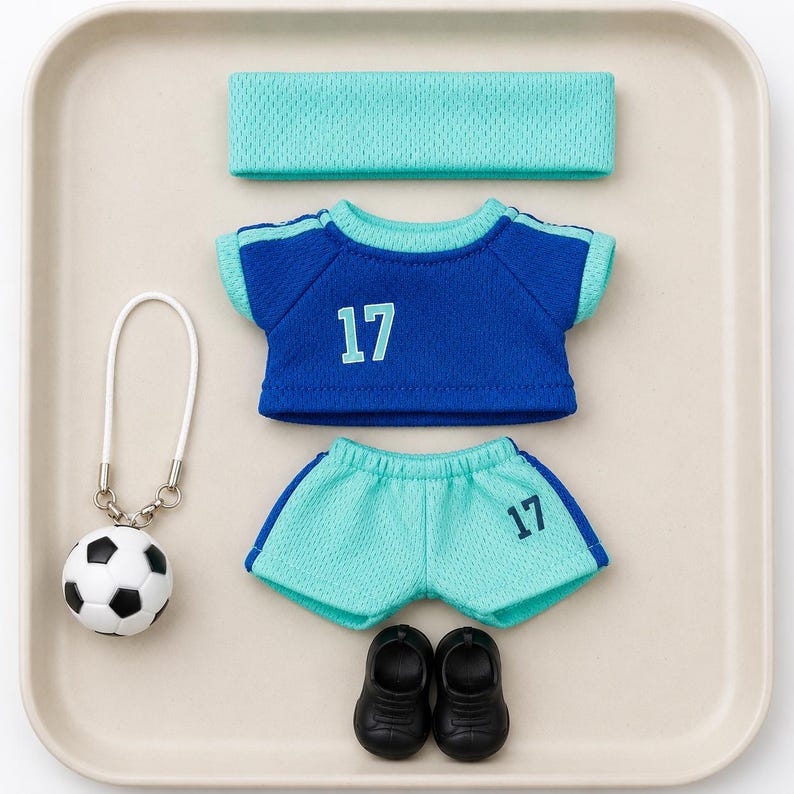 May include: A doll-sized sports outfit featuring a blue t-shirt with the number 17 in light blue, light blue mesh shorts with the number 17 in dark blue, a matching light blue mesh headband, a pair of black shoes, and a football key ring.