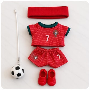 May include: A red headband, a red and green football shirt with the number 7 and a crest, matching red shorts with the number 7 and a crest, a pair of red shoes, and a small black and white football attached to a white cord.