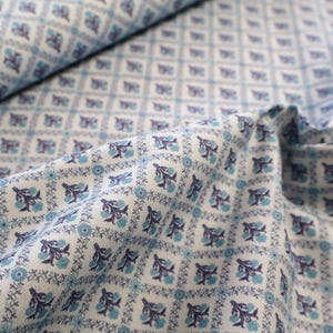 Könnte beinhalten: Ein weißer Stoff mit einem sich wiederholenden Gittermuster aus hellblauen und dunkelblauen Blumenmotiven. Das Design besteht aus kleinen, stilisierten Blüten und feinen, rankenartigen Details, die in quadratischen Abschnitten angeordnet sind.