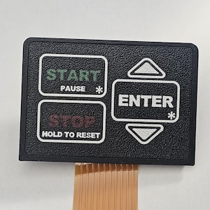 May include: A rectangular black control panel overlay with a textured surface. It features white outlined buttons labeled START PAUSE, STOP HOLD TO RESET, and ENTER with up and down arrows. A flexible orange ribbon cable extends from the bottom edge.