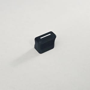 May include: A small, black, rectangular object with a white stripe on top. The object has a ridged texture on its sides and is set against a plain white background. The item appears to be a small electronic component or a similar product.