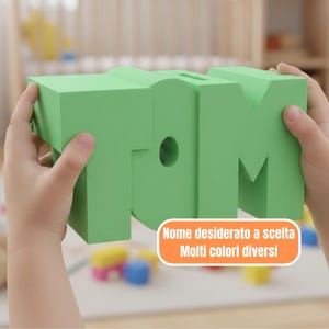 Könnte beinhalten: Ein grüner Schaumstoffblock mit dem Namen "TOM". Die Buchstaben sind dick und dreidimensional, mit einem kreisförmigen Loch im Buchstaben "O". Der Text "Nome desiderato a scelta Molti colori diversi" ist enthalten.