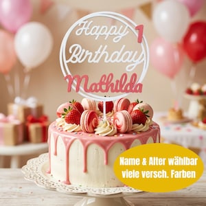 Könnte beinhalten: Ein runder Kuchen mit rosa Glasur, verziert mit frischen Erdbeeren und Macarons. Ein weißer, kreisförmiger Tortenstecker mit der Aufschrift Happy Birthday, der Zahl 1 und dem Namen Mathilda in rosa Schreibschrift steckt oben auf dem Kuchen.