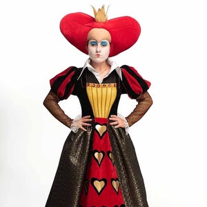 May include: A Queen of Hearts costume from Alice in Wonderland. The dress is black, red, and gold, with heart-shaped details. The headpiece is a large red heart with a gold crown. The sleeves are black and red.