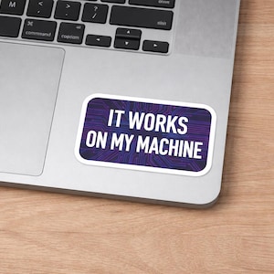 Puede incluir: Una pegatina con borde blanco con el texto "IT WORKS ON MY MACHINE" en letras blancas. La pegatina tiene un fondo de diseño de placa de circuito púrpura y azul. La pegatina está colocada en un portátil plateado.