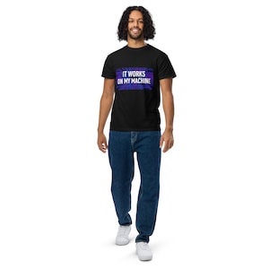 May include: A black short-sleeved t-shirt featuring a rectangular graphic with a purple and blue circuit board pattern and the white text IT WORKS ON MY MACHINE centred on the chest, paired with blue denim jeans and white trainers.