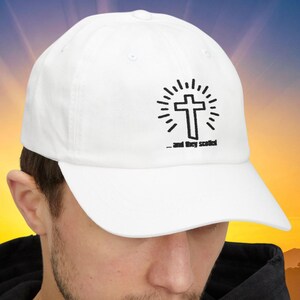May include: White baseball cap featuring a black cross design with radiating lines and the text "...and they scoffed." The cap has a curved brim and is made of a soft fabric. A stylish accessory for everyday wear.