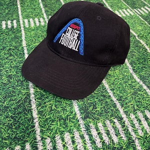 May include: Black baseball cap featuring the ESPN College Football logo in white and blue. The cap has a curved brim and a structured crown. The background is a green field with white yard lines.