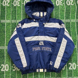 May include: A navy blue and gray Penn State hooded jacket. The jacket features the words "PENN STATE" across the front, with a logo above. The jacket has a drawstring hood, a front pocket, and gray stripes across the chest and sleeves.
