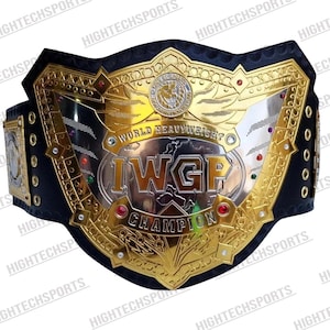 Puede incluir: Un cinturón de campeonato dorado y plateado con el texto "WORLD HEAVYWEIGHT IWGP CHAMPION". El cinturón tiene una correa de cuero negro y está adornado con detalles dorados y piedras preciosas rojas. Es un trofeo deportivo.