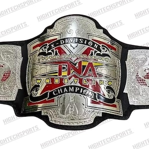 Puede incluir: Un cinturón de campeonato de lucha libre con un diseño plateado y negro. El cinturón presenta el texto "X-DIVISION" y "TNA WRESTLING CHAMPION". La placa central tiene detalles en rojo y amarillo. Las placas laterales tienen un diseño de globo.
