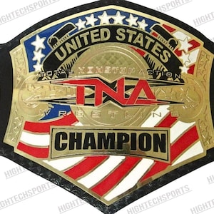Puede incluir: Un cinturón de campeonato de lucha libre dorado y negro. El cinturón presenta el texto "UNITED STATES" y "CHAMPION" con detalles en rojo, blanco y azul. También se puede ver el texto "TNA Wrestling".