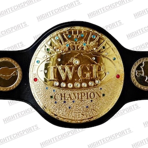 Puede incluir: Un cinturón de campeonato de lucha libre dorado con las letras "IWGP" en relieve. El cinturón tiene una correa de cuero negro y está adornado con joyas y la palabra "CHAMPION".