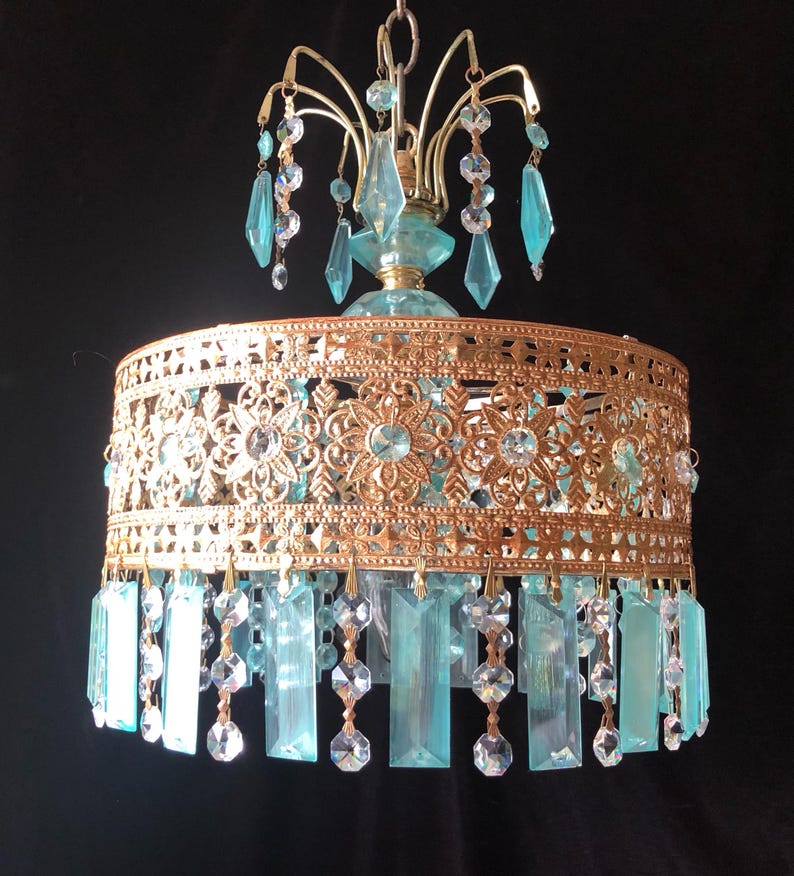 May include: A vintage chandelier with a gold-colored filigree shade and hanging blue-green crystal accents. The chandelier has a decorative top with additional crystal embellishments, creating a glamorous lighting fixture.