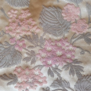 May include: Close-up of a beige fabric with a floral pattern. The fabric features pink flowers and gray leaves.