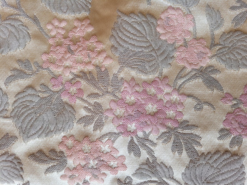 May include: Close-up of a beige fabric with a floral pattern. The fabric features pink flowers and gray leaves.