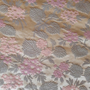 May include: Beige fabric with a repeating pattern of pink flowers and gray leaves.
