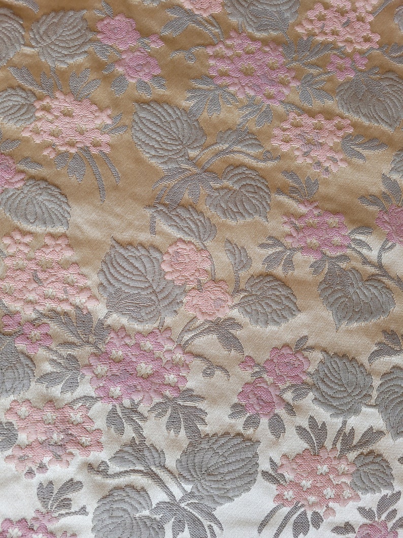 May include: Beige fabric with a repeating pattern of pink flowers and gray leaves.