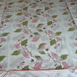 May include: A white bedspread with a pink and green floral pattern. The bedspread has a pink ruffled border.