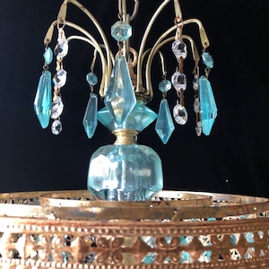 May include: Vintage chandelier with a brass frame and light blue and clear crystal accents. The chandelier features a central light blue glass element and hanging crystal pendants. The design includes a decorative brass base.