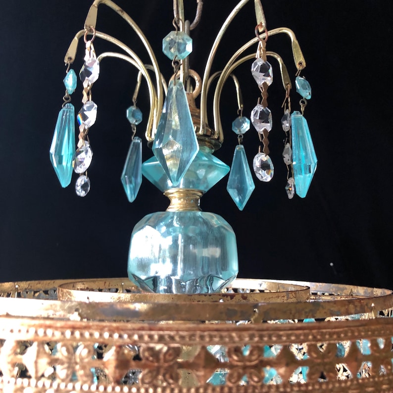 May include: Vintage chandelier with a brass frame and light blue and clear crystal accents. The chandelier features a central light blue glass element and hanging crystal pendants. The design includes a decorative brass base.