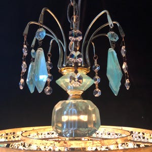 May include: An antique chandelier with a gold-toned metal frame and hanging crystal accents. The chandelier features light blue glass pendants and clear crystal droplets, creating a vintage aesthetic. The fixture is suspended from a chain.