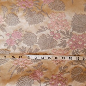May include: Close-up of a beige fabric with a pink and gray floral pattern. A measuring tape is placed across the fabric, showing measurements from 7 to 22 inches.