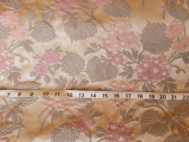 May include: Close-up of a beige fabric with a pink and gray floral pattern. A measuring tape is placed across the fabric, showing measurements from 7 to 22 inches.