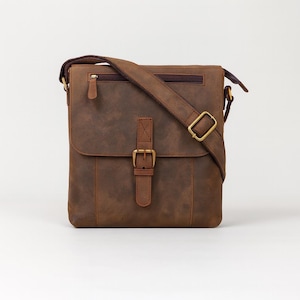 May include: A brown leather messenger bag with a flap closure and adjustable shoulder strap. The bag features a buckle closure, a front pocket, and a zippered top. The bag is approximately 12 inches wide and 10 inches tall.