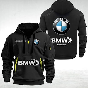 Puede incluir: Sudadera con capucha negra con el logotipo de BMW en la parte delantera y trasera. La parte delantera tiene una cremallera media con detalles amarillos y el logotipo de BMW. La parte trasera muestra el logotipo de BMW y el texto "BMW Since 1916".