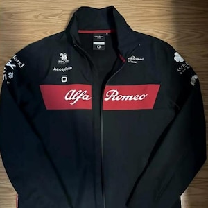 Könnte beinhalten: Schwarze Alfa Romeo Jacke mit rotem Streifen auf der Brust. Die Jacke hat einen durchgehenden Reißverschluss, einen Stehkragen und verschiedene Logos und Texte, darunter "Alfa Romeo" und "Get Closer".