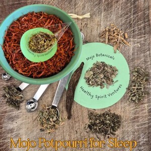 Può includere: Una ciotola turchese piena di erbe arancioni sminuzzate, un piccolo cucchiaio verde e cucchiai dosatori. È presente anche un cerchio verde con testo e varie erbe essiccate. Il testo "Mojo Potpourri for Sleep" è in basso.