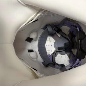 May include: White safety helmet with interior suspension system. The interior features a gray and purple harness, black straps, and a black adjustment knob. The helmet is designed for head protection.