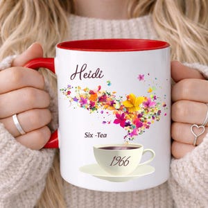 May include: White ceramic mug with a red interior and handle. The mug features the name "Heidi" in cursive, a colorful floral design, and the text "Six -Tea" and "1966".